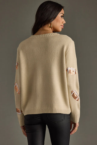 Woman wearing a beige sweater with floral patterns on a gray background
